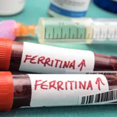 Dwie probówki z krwią oznaczone "Ferritina" i strzałką w górę, sugerujące potrzebę podniesienia ferrytyny. W tle strzykawka i fiolki.