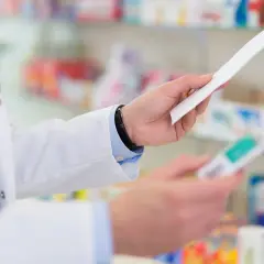 Farmaceuta w białym fartuchu trzyma receptę i opakowanie leku, być może Laxigen, w aptece.