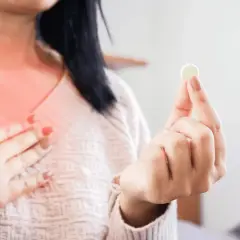 Kobieta z pieczeniem w klatce piersiowej trzyma tabletkę, zastanawiając się: ipp co to za lek?