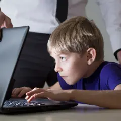 Chłopiec pochłonięty grą na laptopie, a dorosły próbuje go odciągnąć. Czy to początek uzależnienia od internetu?
