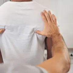 Fizjoterapeuta bada plecy pacjenta w białej koszulce.