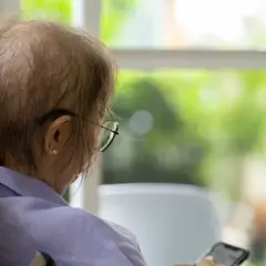 Osoba po chemioterapii w okularach siedzi przy oknie, trzymając telefon.