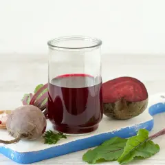 Szklanka z intensywnym, rubinowym sokiem z kiszonych buraków, obok świeże buraki i przyprawy. Zdrowie w płynie!