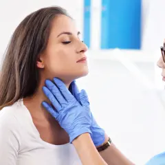 Lekarz w niebieskich rękawiczkach bada szyję pacjentki, przygotowując ją do scyntygrafii tarczycy.