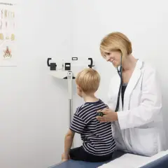Lekarka osłuchuje chłopca podczas bilansu dziecka. W tle waga lekarska i plakat z kręgosłupem.
