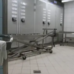 Wnętrze prosektorium: wózek do transportu, szafy chłodnicze i rękawiczka na uchwycie stołu.