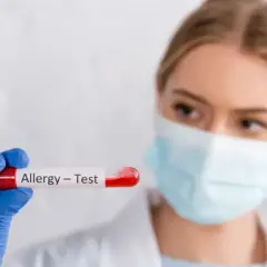 Ręka w niebieskiej rękawiczce trzyma probówkę z krwią do testów alergicznych.