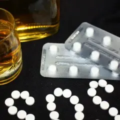 Szklanka alkoholu i blistry z tabletkami, które mogą być benzodiazepiny, ułożone w napis SOS.