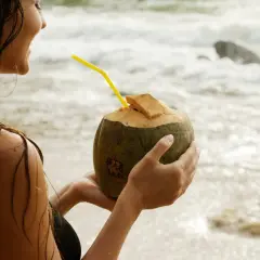 Kobieta na plaży pije wodę kokosową, doceniając jej orzeźwiające właściwości.