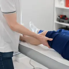 Fizjoterapeuta wykonuje masaż nogi pacjenta leżącego na kozetce.