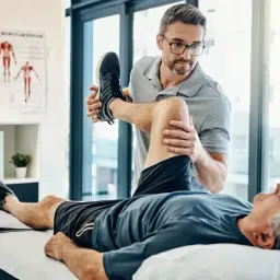 Fizjoterapeuta pomaga starszemu mężczyźnie w ćwiczeniach. Dobre ubezpieczenie zdrowotne zapewnia dostęp do takiej rehabilitacji.