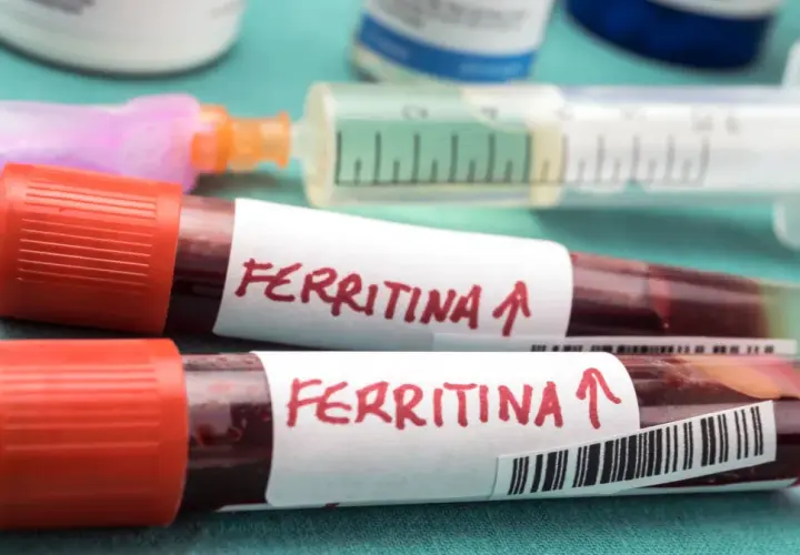 Dwie probówki z krwią oznaczone "Ferritina" i strzałką w górę, sugerujące potrzebę podniesienia ferrytyny. W tle strzykawka i fiolki.