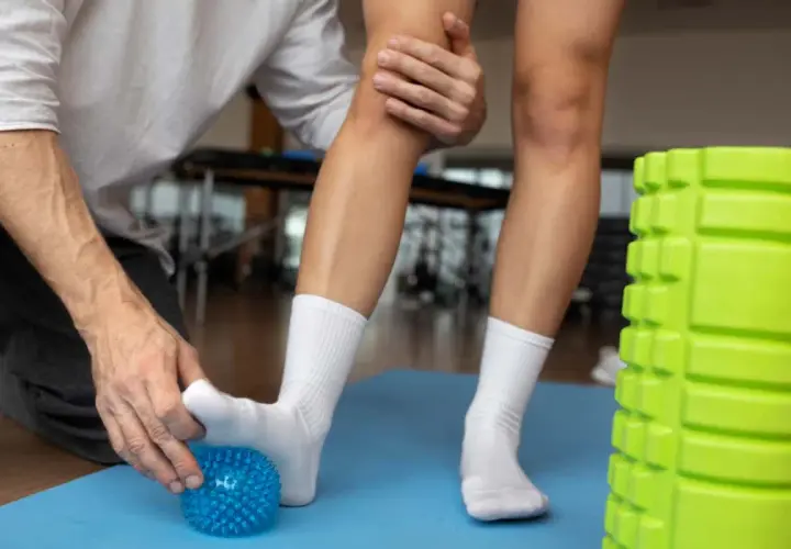 Rehabilitacja stawu skokowego: masaż stopy niebieską piłeczką, pomoc terapeuty.