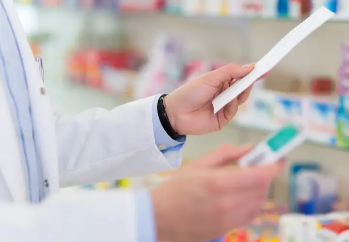 Farmaceuta w białym fartuchu trzyma receptę i opakowanie leku, być może Laxigen, w aptece.