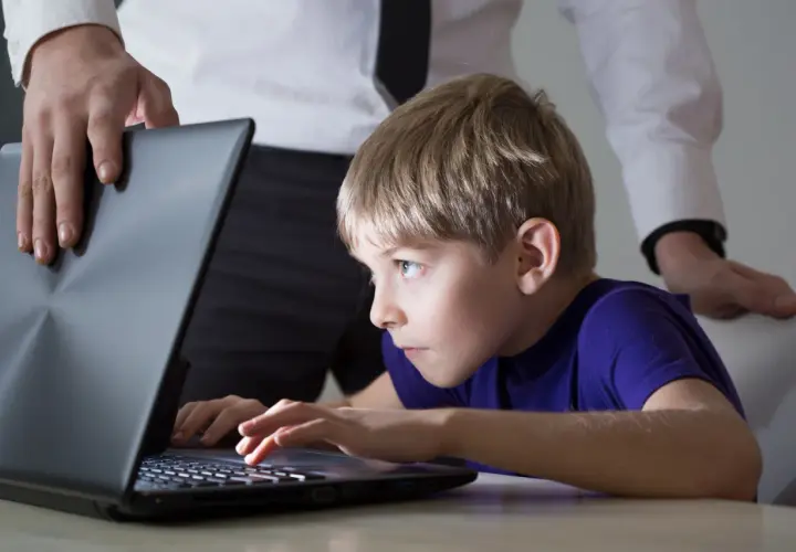 Chłopiec pochłonięty grą na laptopie, a dorosły próbuje go odciągnąć. Czy to początek uzależnienia od internetu?