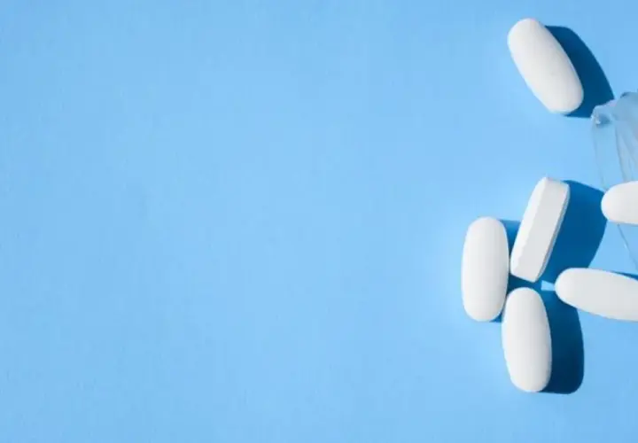 Białe tabletki, w tym oxycodone, wysypują się z przezroczystego pojemnika na niebieskim tle.