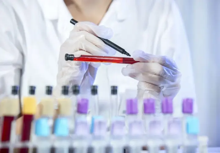 Laborant w rękawiczkach trzyma probówkę z czerwoną cieczą i pisak.