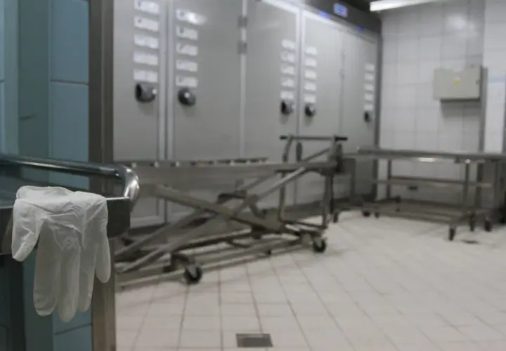 Wnętrze prosektorium: wózek do transportu, szafy chłodnicze i rękawiczka na uchwycie stołu.