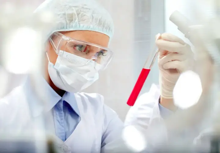 Naukowczyni w okularach i masce bada czerwoną ciecz w probówce. Czy to początek badań nad PCT?