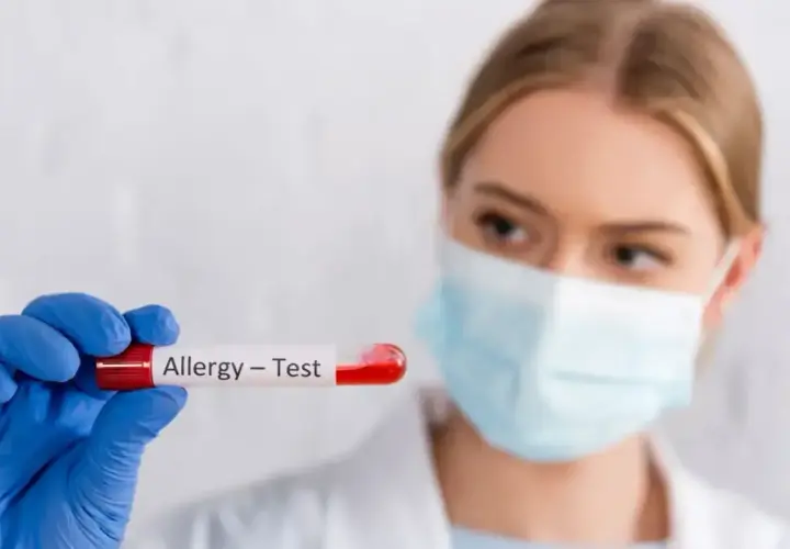 Ręka w niebieskiej rękawiczce trzyma probówkę z krwią do testów alergicznych.