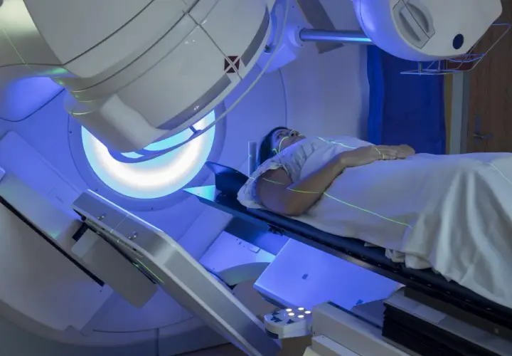 Pacjentka leży na stole terapeutycznym pod aparatem do radioterapii. Zielone linie laserowe wyznaczają pole napromieniania. To przykład, jak wygląda radioterapia co to za leczenie.