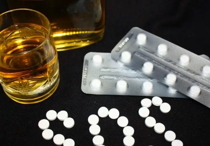 Szklanka alkoholu i blistry z tabletkami, które mogą być benzodiazepiny, ułożone w napis SOS.