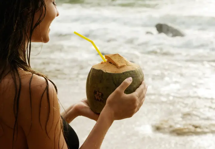 Kobieta na plaży pije wodę kokosową, doceniając jej orzeźwiające właściwości.