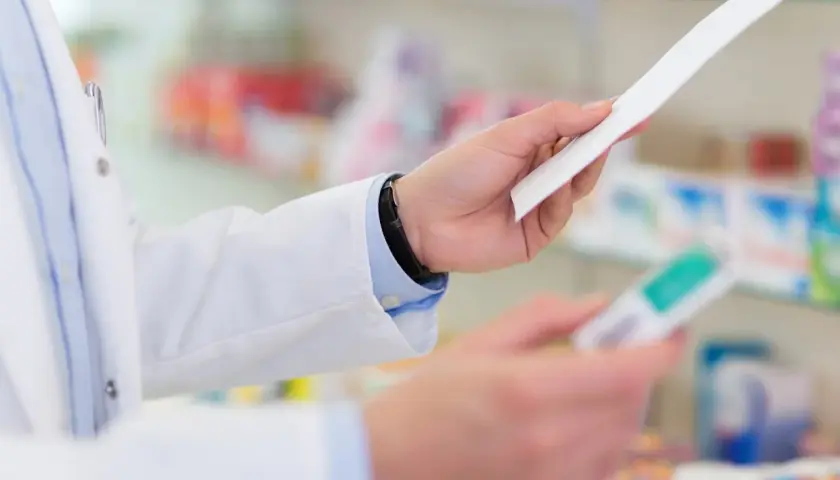 Farmaceuta w białym fartuchu trzyma receptę i opakowanie leku, być może Laxigen, w aptece.