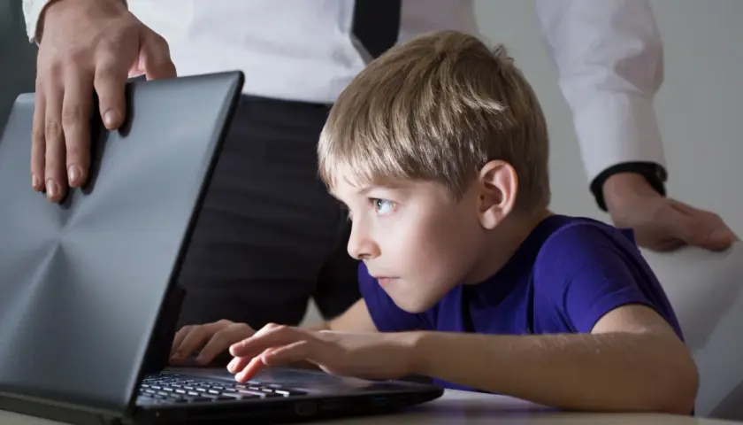 Chłopiec pochłonięty grą na laptopie, a dorosły próbuje go odciągnąć. Czy to początek uzależnienia od internetu?