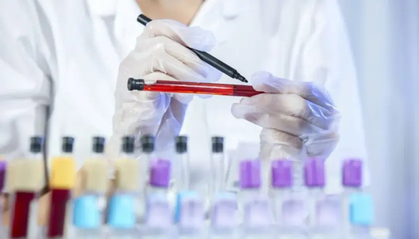 Laborant w rękawiczkach trzyma probówkę z czerwoną cieczą i pisak.