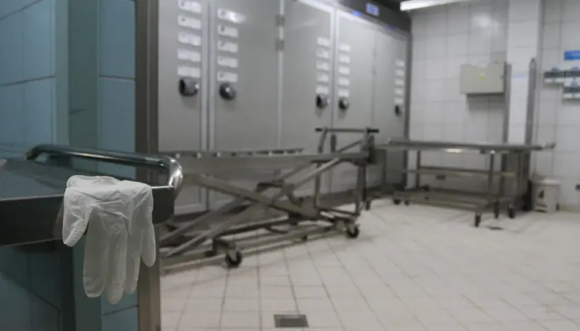 Wnętrze prosektorium: wózek do transportu, szafy chłodnicze i rękawiczka na uchwycie stołu.