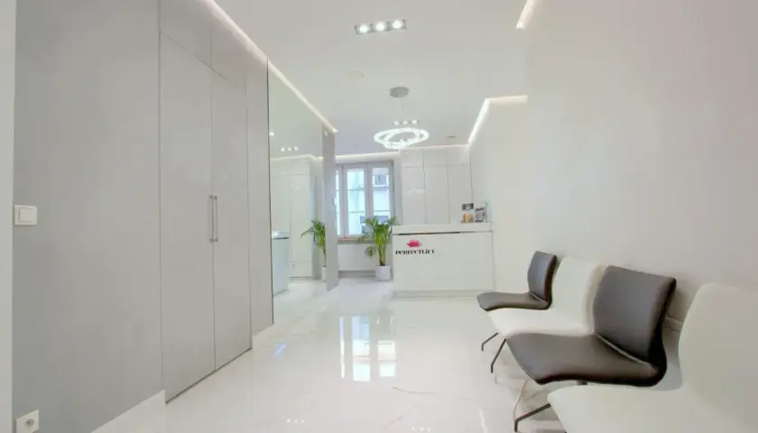 Nowoczesne wnętrze poczekalni kliniki estetycznej z białym marmurem i wygodnymi fotelami.