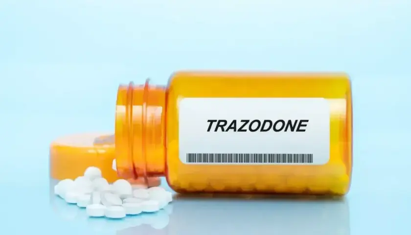 Pomarańczowa buteleczka leku trazodon, z której wysypały się białe tabletki.