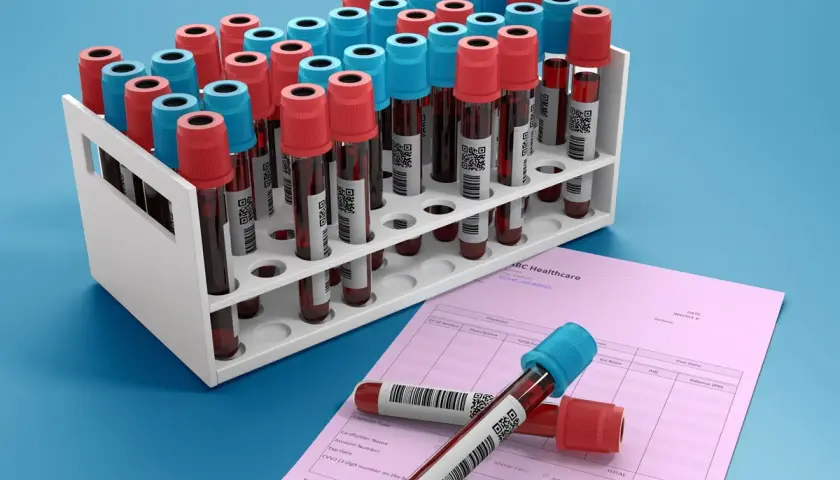Rząd probówek z krwią, niektóre z czerwonymi, inne z niebieskimi nakrętkami, stoją w białym stojaku. Obok leży różowa faktura ABC Healthcare. Ca 15-3.