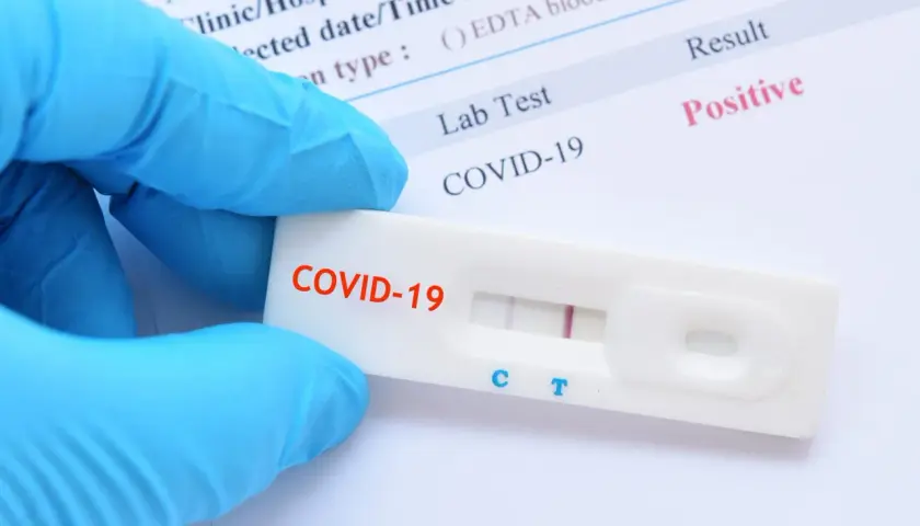 Rękawiczka w niebieskiej rękawiczce trzyma test na COVID-19 z pozytywnym wynikiem. Zastanawiasz się, ile kosztuje test na COVID?
