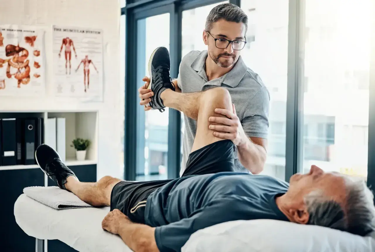Fizjoterapeuta pomaga starszemu mężczyźnie w ćwiczeniach. Dobre ubezpieczenie zdrowotne zapewnia dostęp do takiej rehabilitacji.