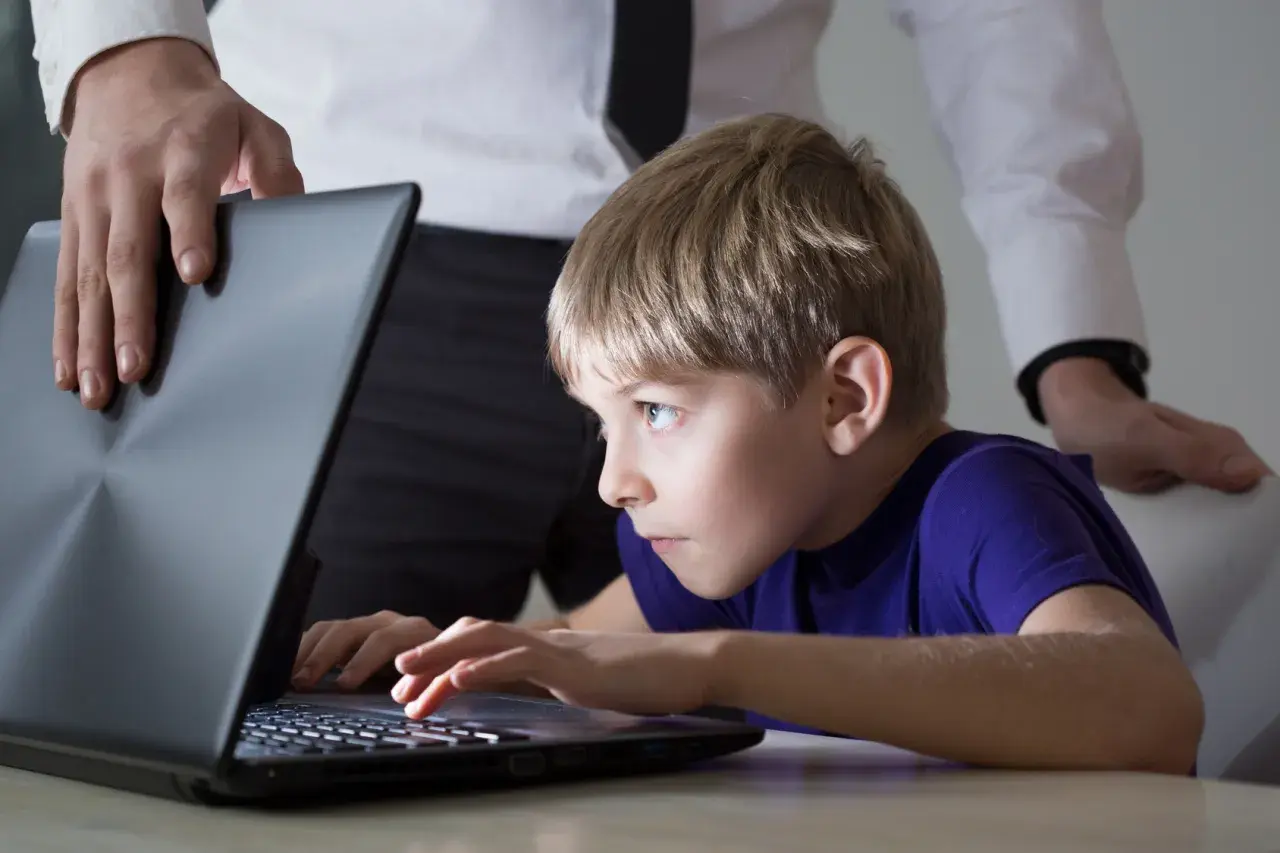 Chłopiec pochłonięty grą na laptopie, a dorosły próbuje go odciągnąć. Czy to początek uzależnienia od internetu?