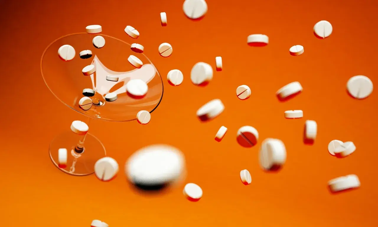 Białe tabletki, w tym Xarelto 20 mg, spadają z kieliszka na pomarańczowym tle.