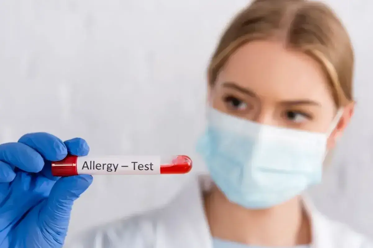 Ręka w niebieskiej rękawiczce trzyma probówkę z krwią do testów alergicznych.