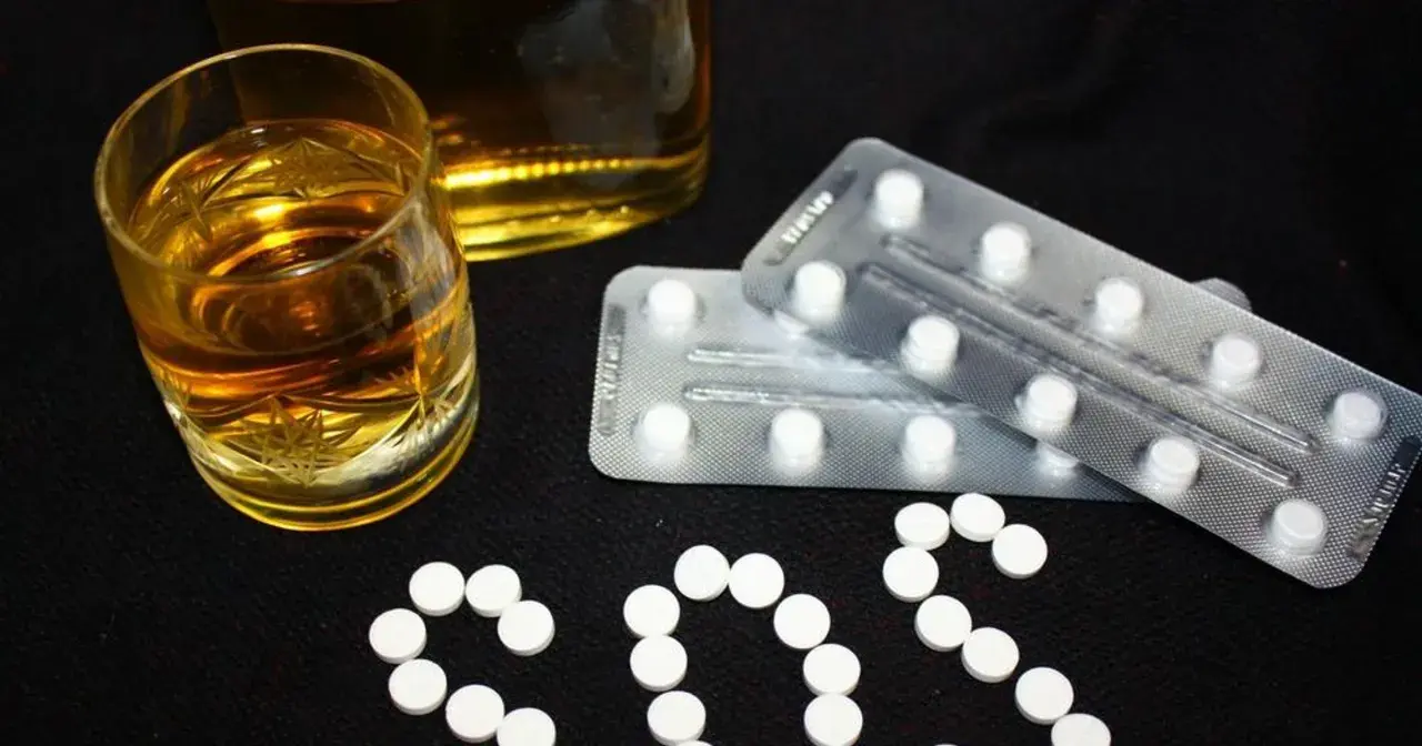 Szklanka alkoholu i blistry z tabletkami, które mogą być benzodiazepiny, ułożone w napis SOS.