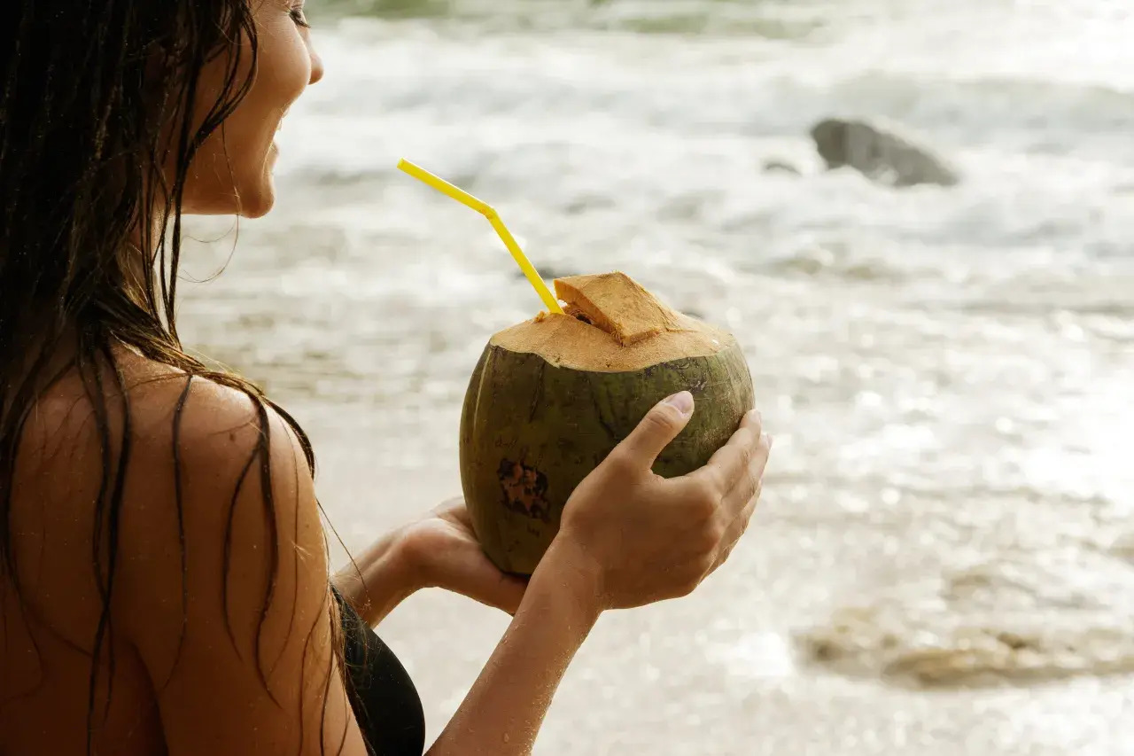 Kobieta na plaży pije wodę kokosową, doceniając jej orzeźwiające właściwości.