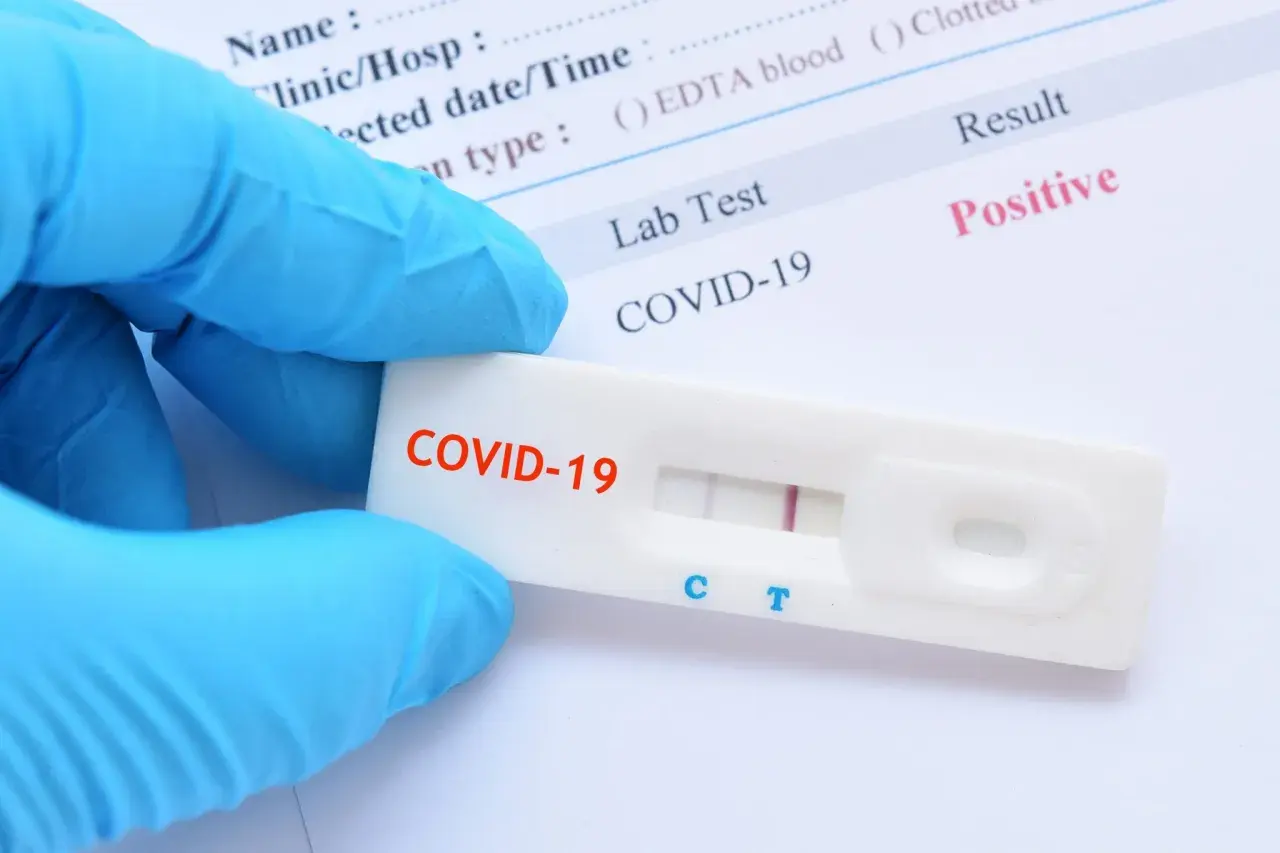Rękawiczka w niebieskiej rękawiczce trzyma test na COVID-19 z pozytywnym wynikiem. Zastanawiasz się, ile kosztuje test na COVID?
