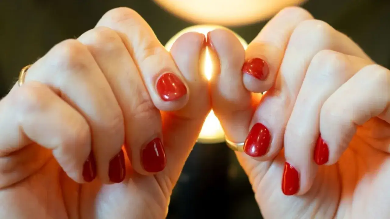 Dłonie z paznokciami pomalowanymi na czerwono, tworzące kształt serca. Palce pałeczkowate, ozdobione błyszczącym lakierem.