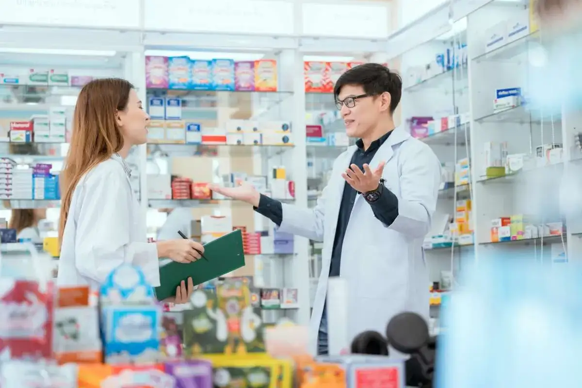Farmaceuta wyjaśnia pacjentce, jak stosować nowy antybiotyk, wskazując na półki z lekami.