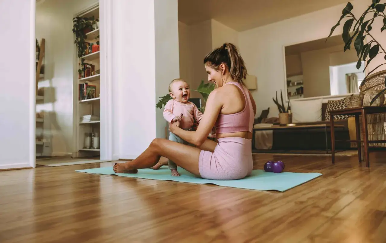 Szczęśliwa mama ćwiczy z dzieckiem, odzyskując formę po ciąży. Radosny maluch śmieje się w ramionach mamy.